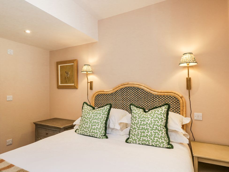 A bedroom with a bed with green patterned pillows and a wicker headboard with bedside tables and lamps at Cedar in Elcot near Newbury