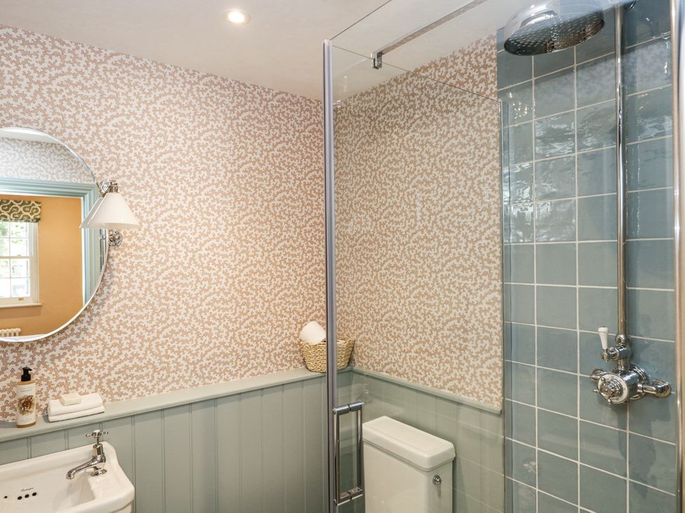 A bathroom with a shower, toilet, sink, round mirror, and patterned wallpaper at Cedar in Elcot near Newbury