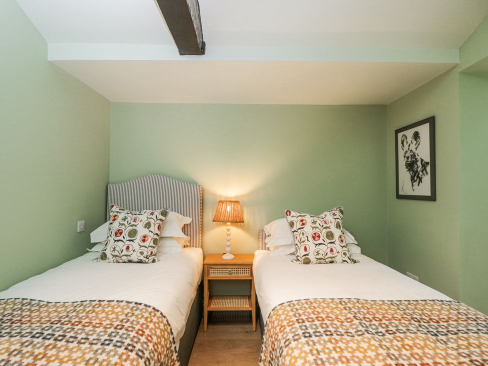 A bedroom with two single beds separated by a nightstand with a lamp and a framed picture on the wall at Cedar Elcot near Newbury