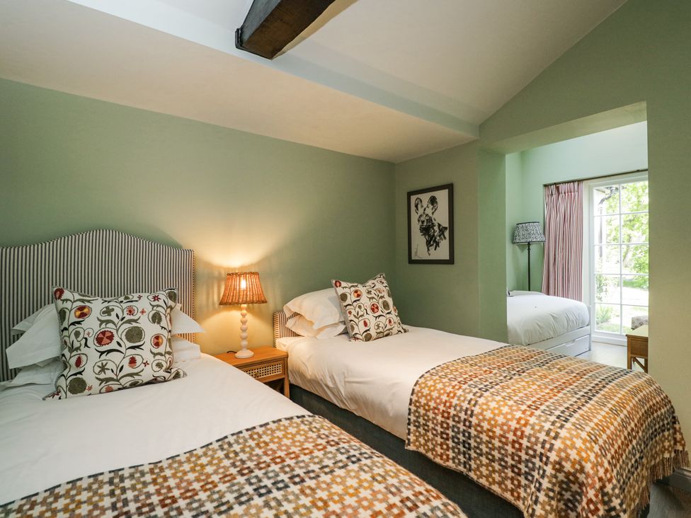 A bedroom with two single beds with patterned pillows and blankets and a bedside lamp at Cedar in Elcot near Newbury