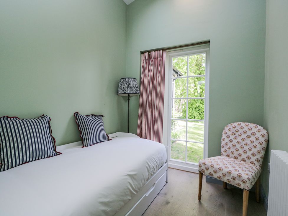 A small bedroom with a bed with striped pillows a floor lamp patterned chair and a window with striped curtains at Cedar in Elcot near Newbury