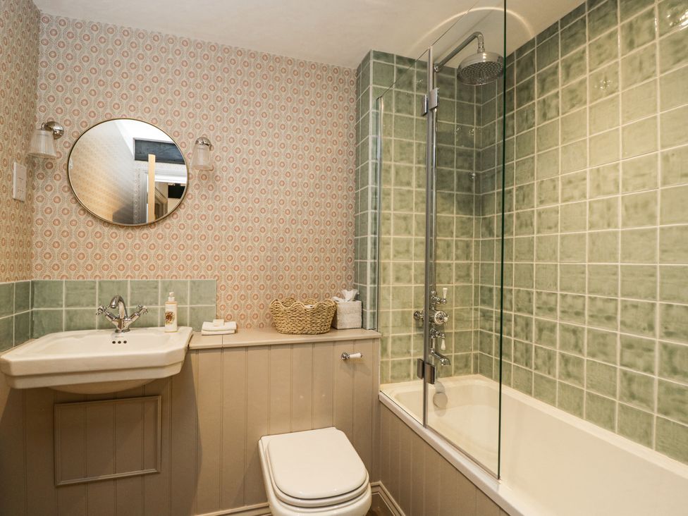 A bathroom with a sink, toilet, bathtub, green tiled walls and a round mirror at Cedar in Elcot near Newbury