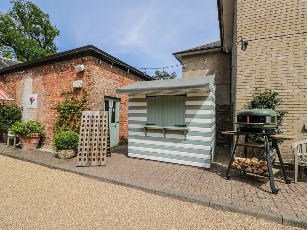 An outdoor area with a green and white striped hut a wooden board with holes a green barbecue and plants at Cedar in Elcot near Newbury