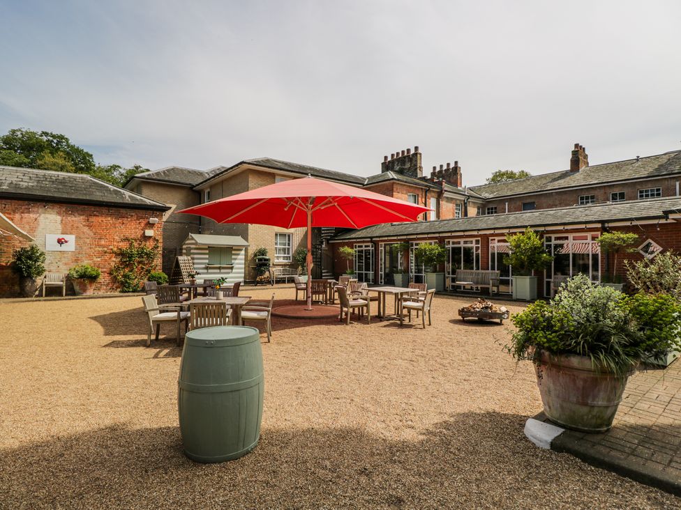 An outdoor seating area with wooden tables and chairs under a large red umbrella and large potted plants at Cedar in Elcot near Newbury