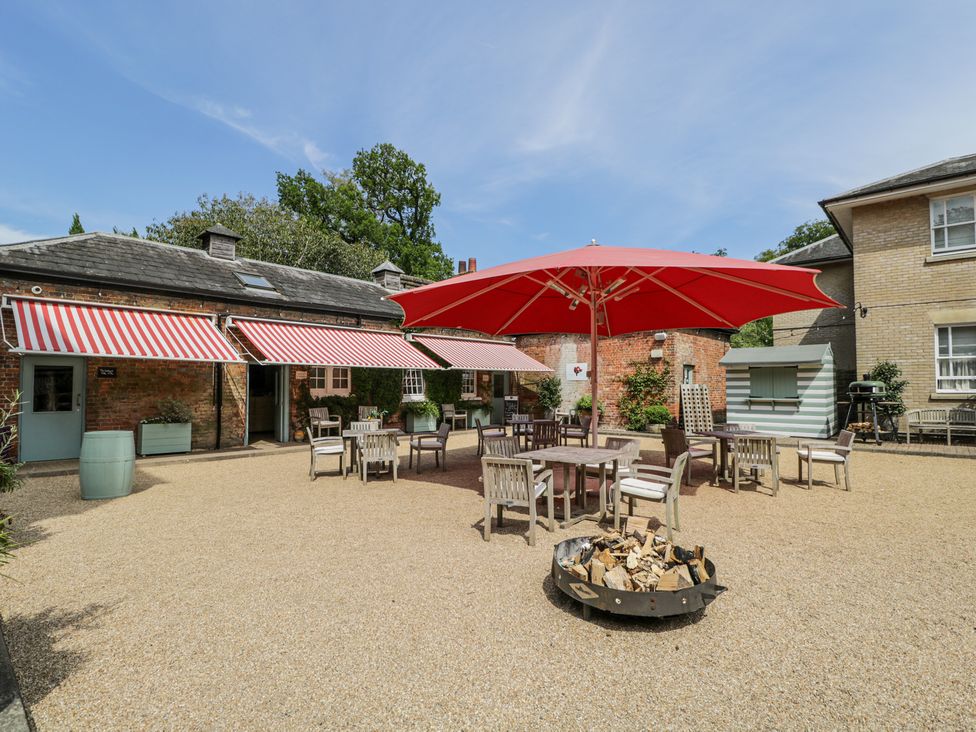 An outdoor courtyard with wooden tables and chairs under a red umbrella and striped awnings on the brick buildings at Cedar in Elcot near Newbury