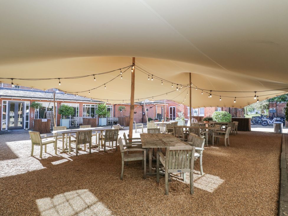 An outdoor seating area with wooden tables and chairs under a beige canopy with string lights at Cedar in Elcot near Newbury