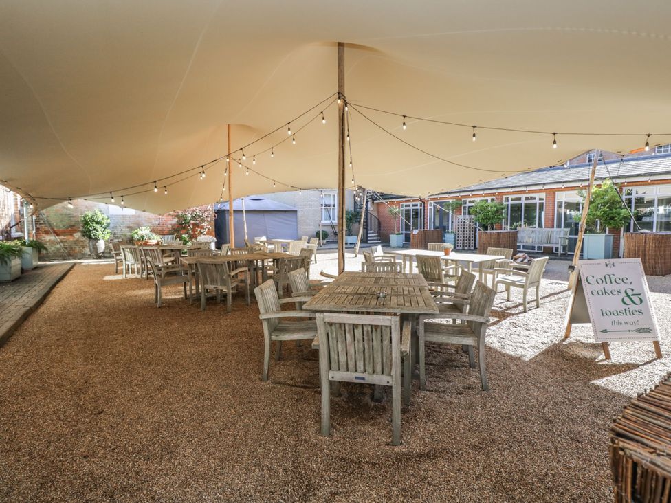 An outdoor seating area with wooden tables and chairs under a canopy with string lights a sign advertising coffee cakes and toasties at Cedar in Elcot near Newbury