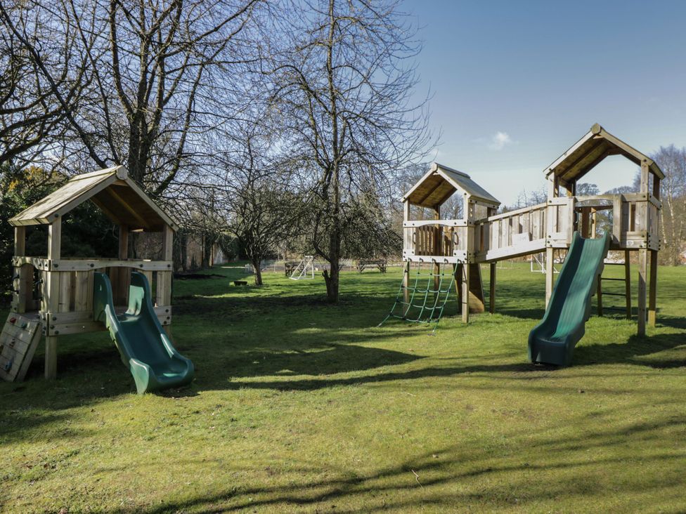 A playground with wooden structures and green slides on grass with trees in the background at Cedar in Elcot near Newbury