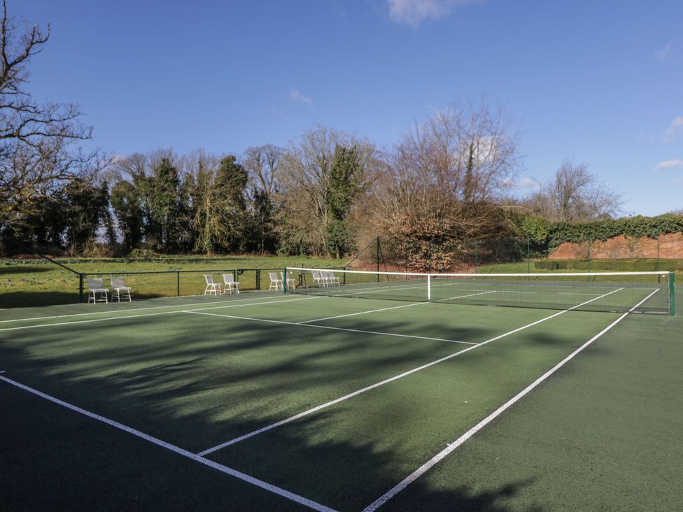 An outdoor tennis court with white chairs along the fence and trees in the background at Cedar Elcot near Newbury