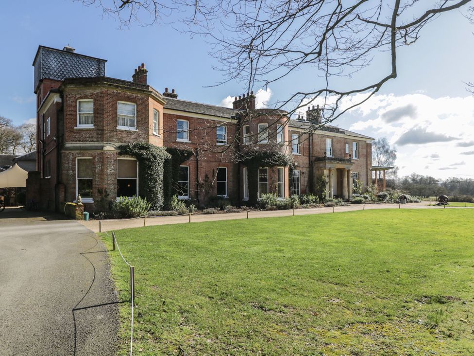 An exterior view of a large brick house with a manicured lawn and tree branches in the foreground at Cedar in Elcot near Newbury