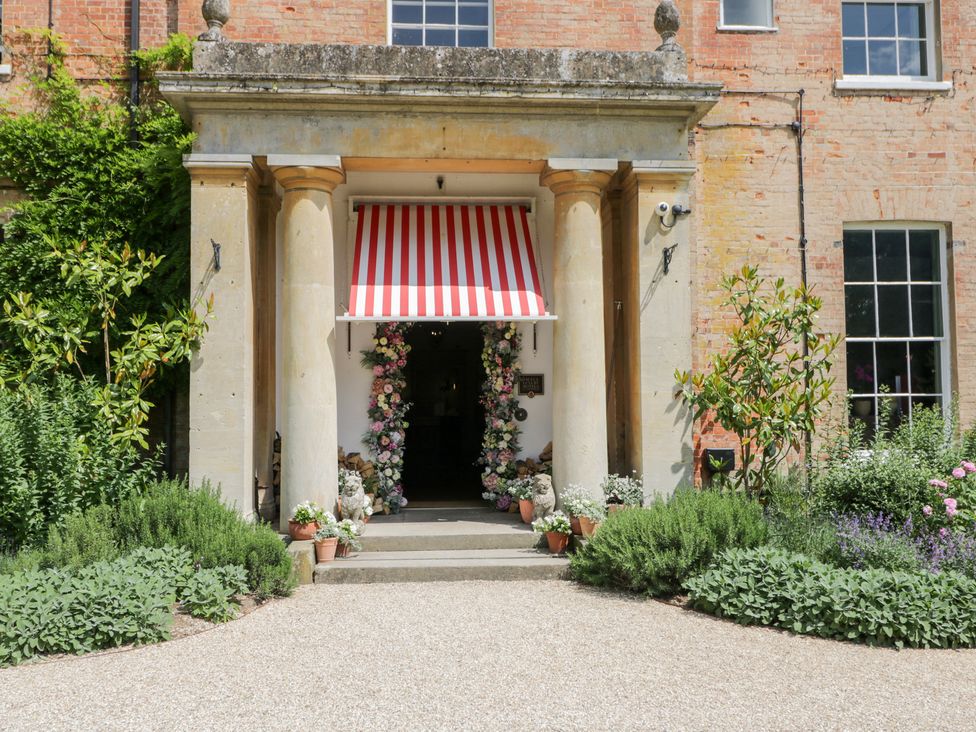 An outdoor entrance with columns, flowers, and a red and white striped awning at Cedar in Elcot near Newbury