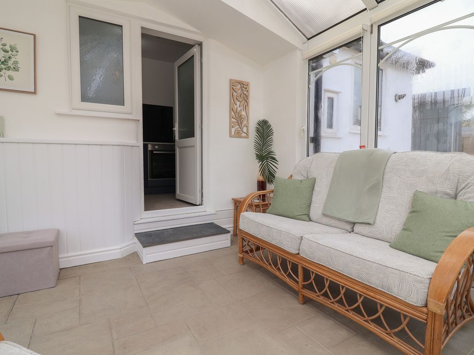 A conservatory with a couch and door leading to a kitchen at Driftwood in Rhyl