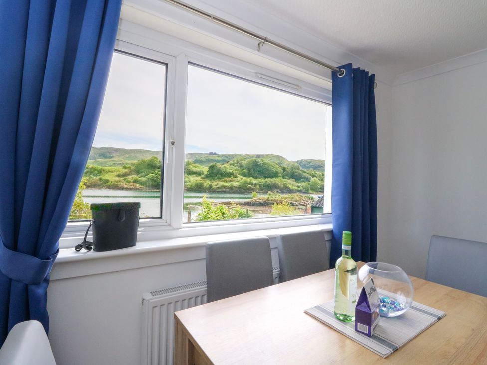 A dining room with a table and a view of the landscape at 3 Whin Bank Clachan-Seil near Balvicar, Isle Of Seil
