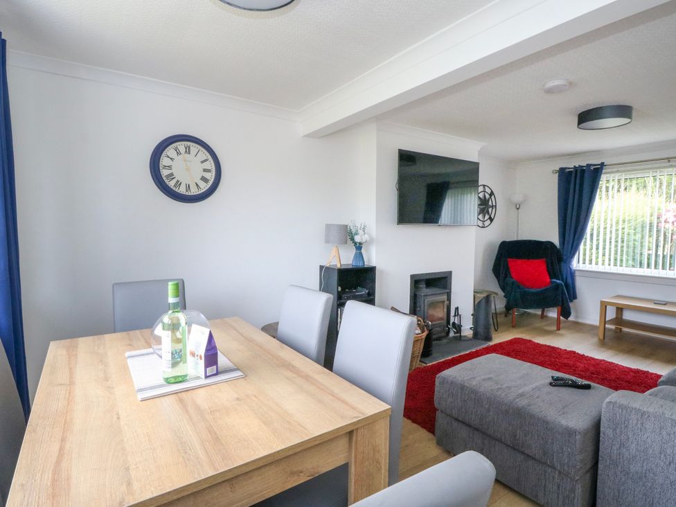 A living room with a dining table and clock at 3 Whin Bank in Clachan-Seil near Balvicar, Isle Of Seil