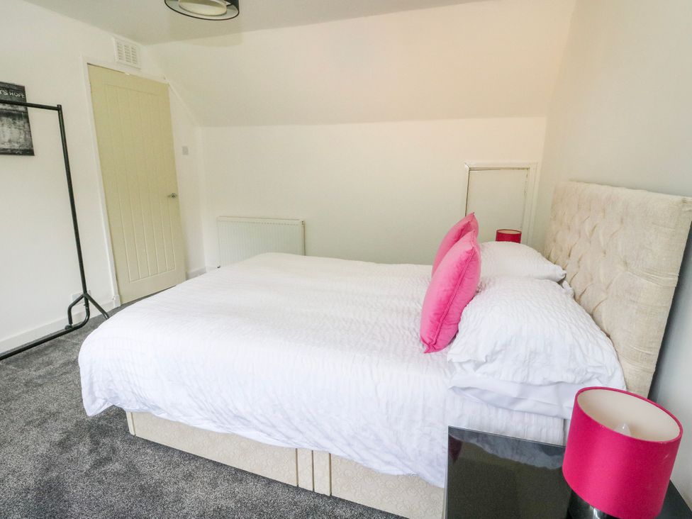 A bedroom with a bed, pink pillows, and a door at 3 Whin Bank Clachan-Seil near Balvicar Isle Of Seil
