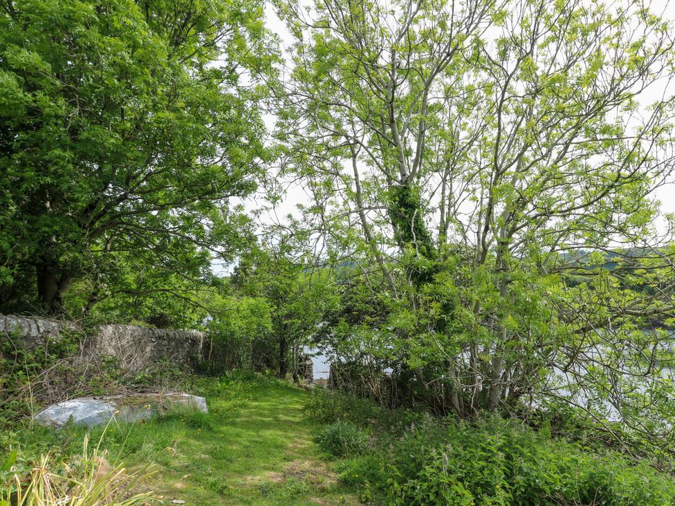 A path leading to water surrounded by trees and bushes at 3 Whin Bank, Clachan-Seil near Balvicar, Isle Of Seil