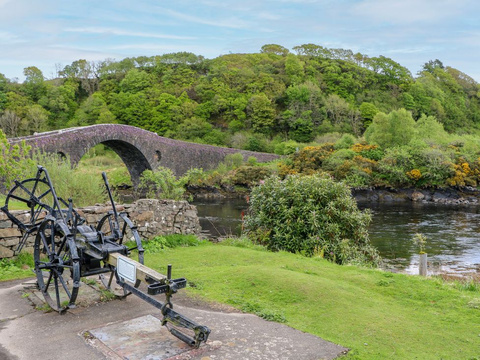 A bridge over a river with a historical artifact in the foreground at 3 Whin Bank Clachan-Seil near Balvicar, Isle Of Seil