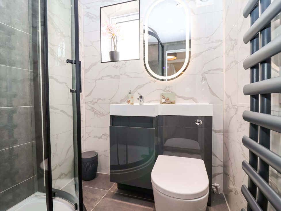 A bathroom with a shower, sink, toilet, and mirror at Lilly's Cottage Dawlish