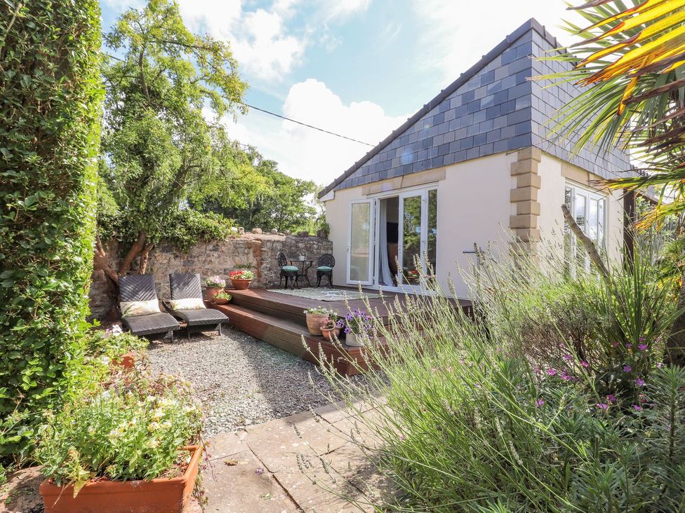 A garden with decking, potted plants, sun loungers, and a table at Mount House Bryniau near Dyserth