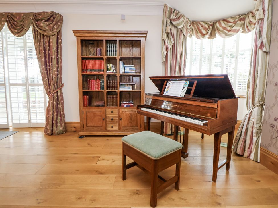 A living room with a piano and bookcase at Mount House Bryniau near Dyserth