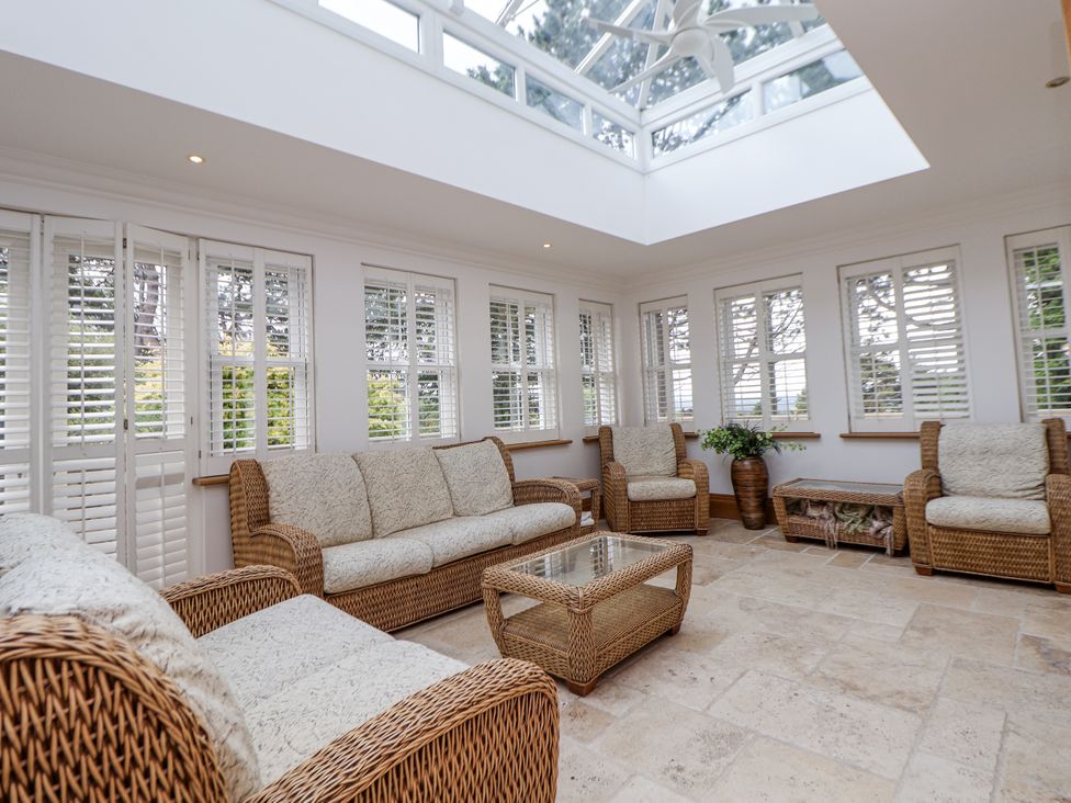 A conservatory with rattan furniture and large windows at Mount House Bryniau near Dyserth