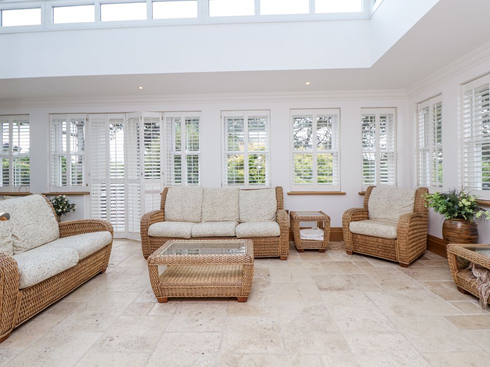 A conservatory with rattan furniture and glass windows at Mount House Bryniau near Dyserth