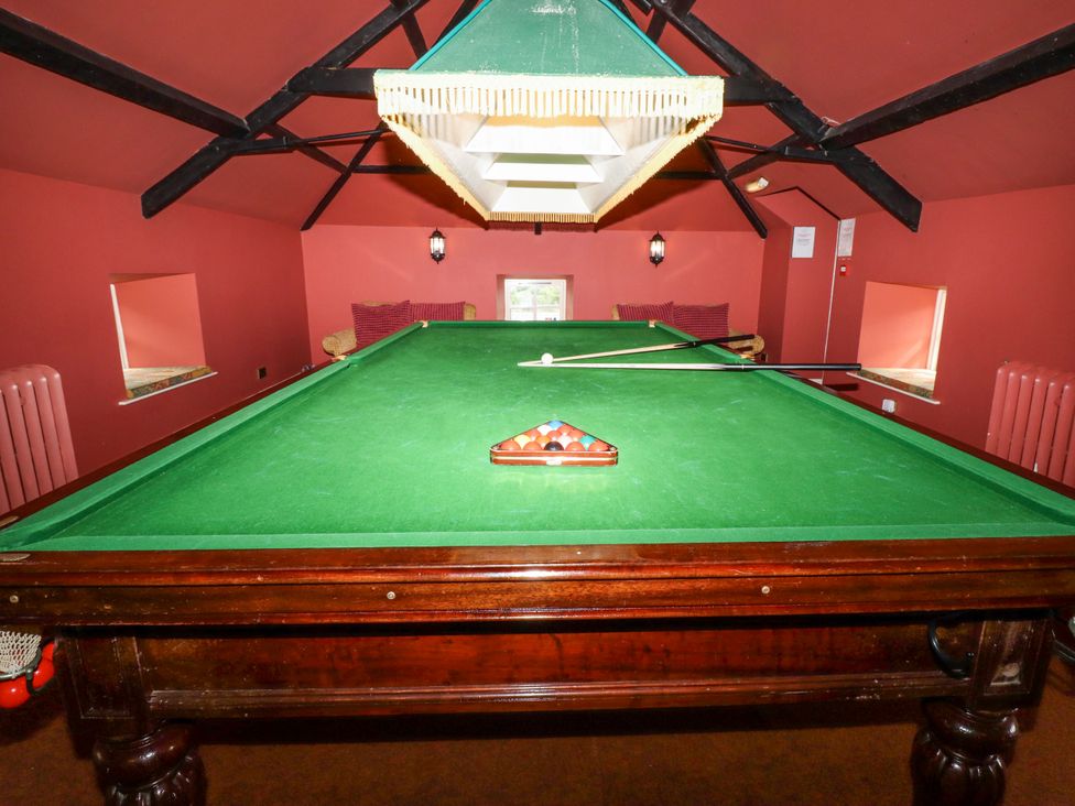 A snooker table with a green lamp above and two cues resting on the table in a room with red walls