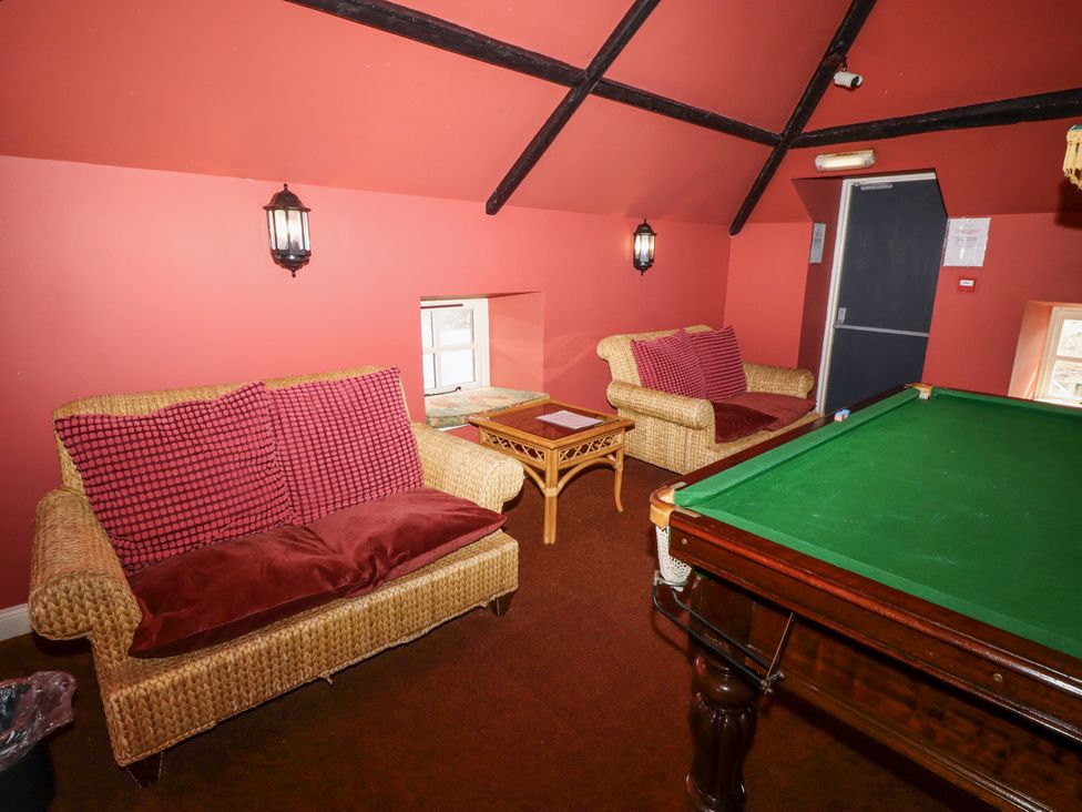 A room with two wicker sofas with red cushions a small wooden table and a pool table at Timberwick Green in Akeld near Wooler
