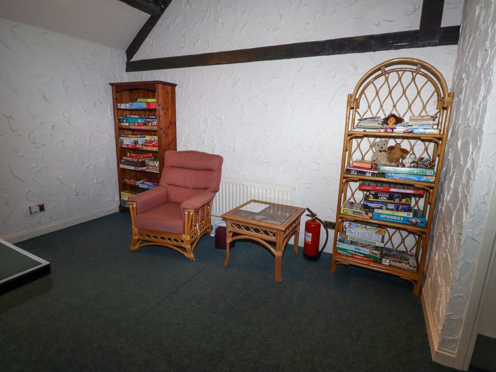 A corner of a room with a red cushioned chair a wooden side table two wooden shelves with board games and toys at Timberwick Green Akeld near Wooler