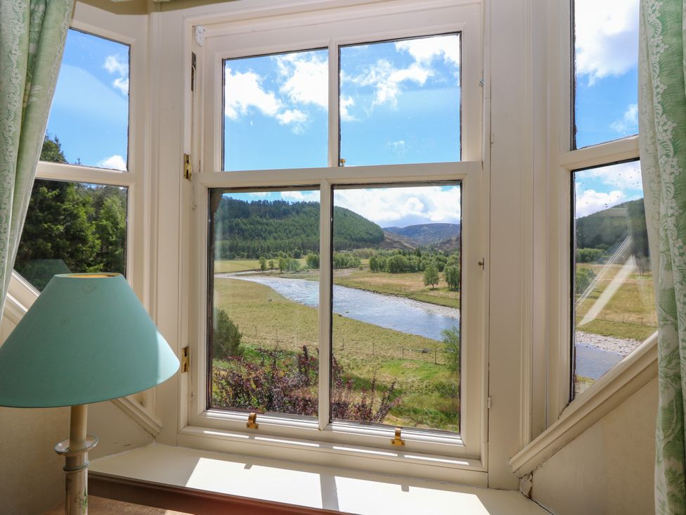 A view from a window with a river and mountains at Claybockie Mar Lodge near Braemar