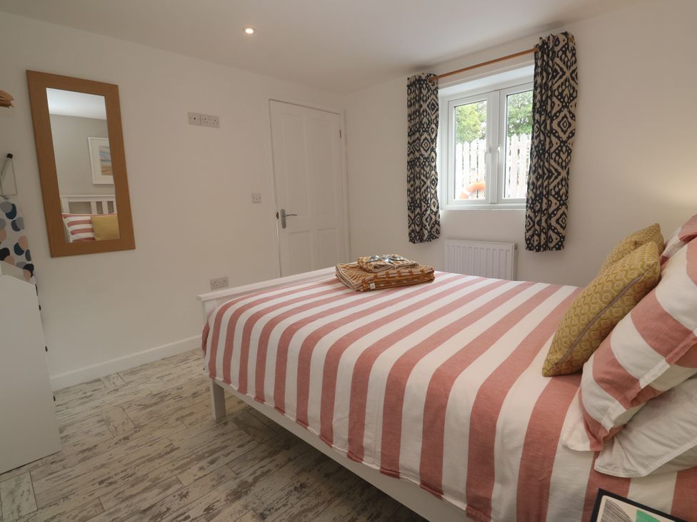 A bedroom with a striped bedspread and a mirror at The Stable in Rosudgeon