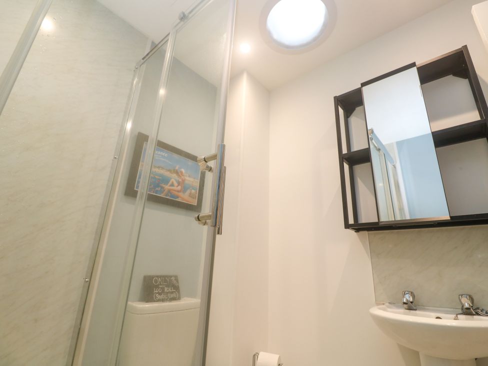 A bathroom with a shower, sink, and storage shelf at Sea View Loft in Rosudgeon