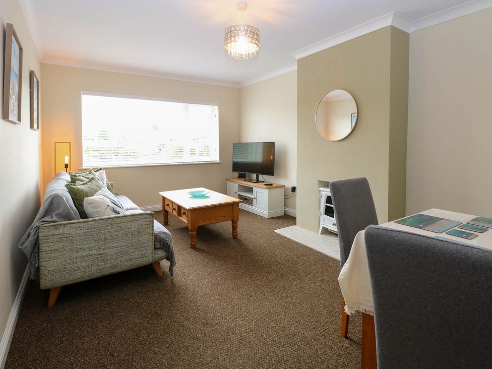 A living room with a sofa a coffee table a TV on a stand a round mirror on the wall and dining chairs at Little Lodge in Dersingham