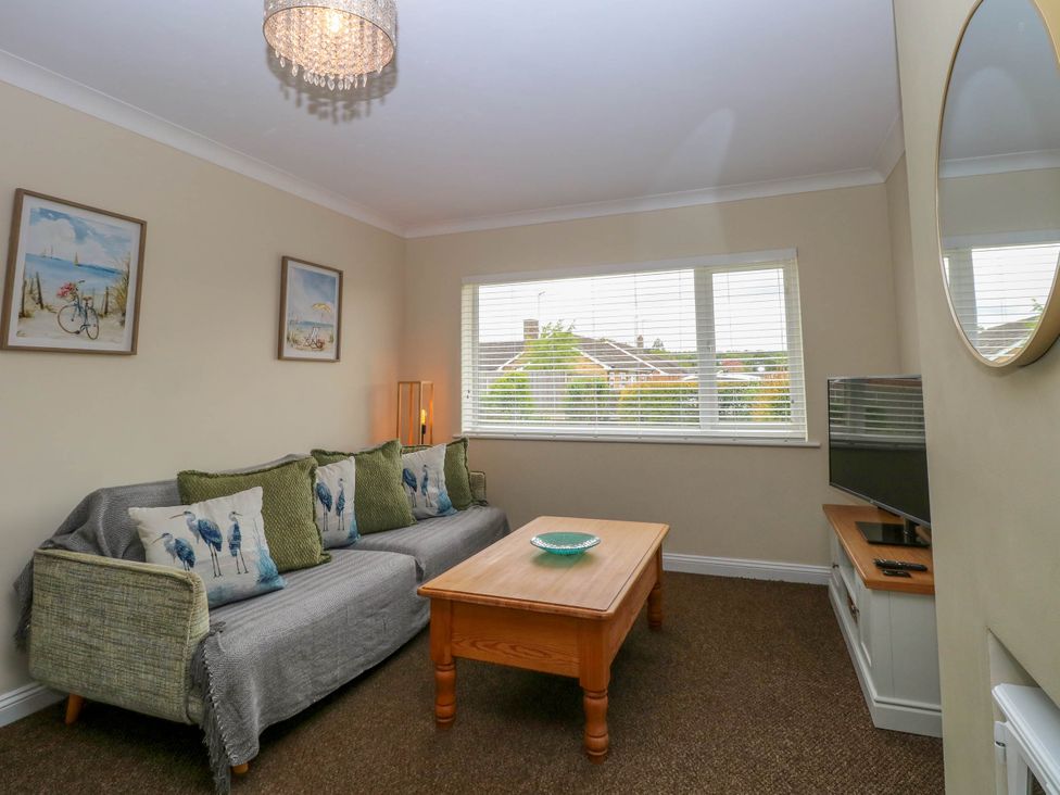 A living room with a sofa with cushions a wooden coffee table a flat screen tv and window blinds at Little Lodge in Dersingham