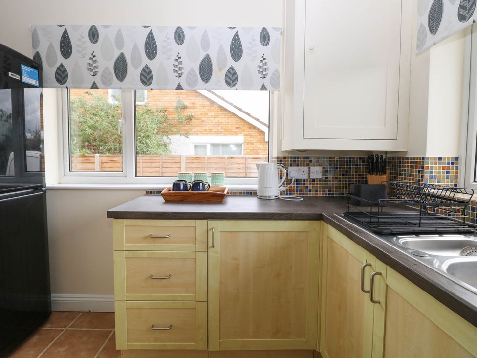 A kitchen with wooden cabinets countertop kettle dish rack and window with patterned blind at Little Lodge in Dersingham