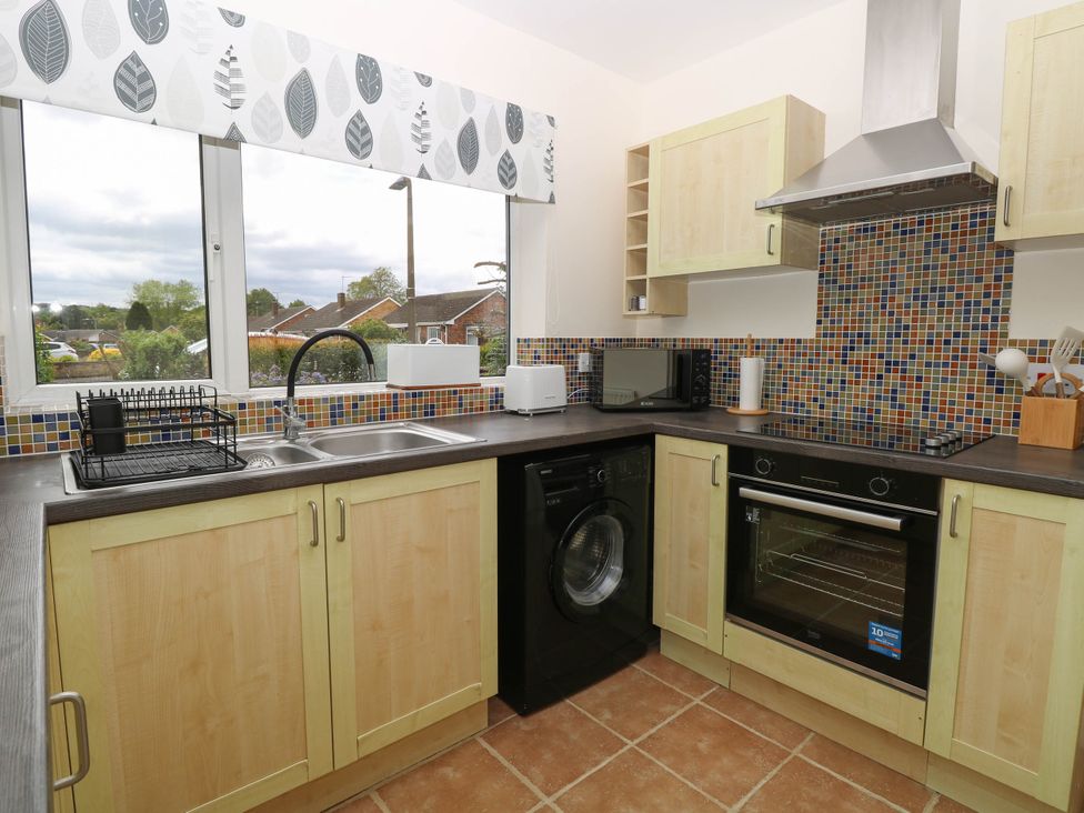 A kitchen with wooden cabinets a double sink a washing machine an oven a microwave and a toaster at Little Lodge in Dersingham