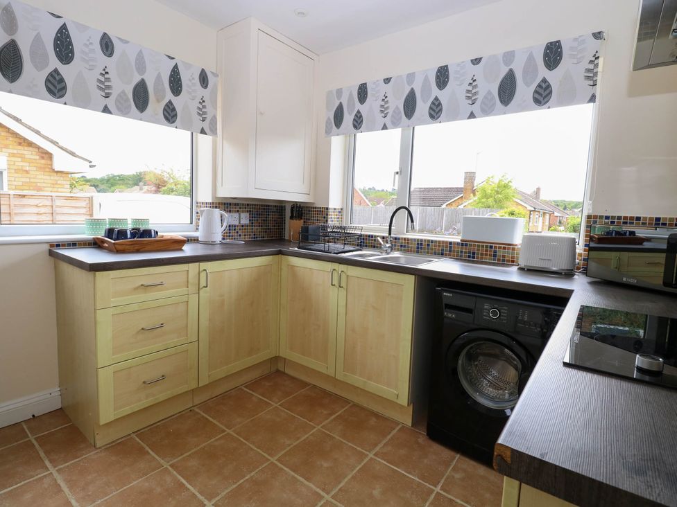 A kitchen with wooden cabinets a washing machine a sink a toaster a microwave a kettle and cups on the counter at Little Lodge in Dersingham