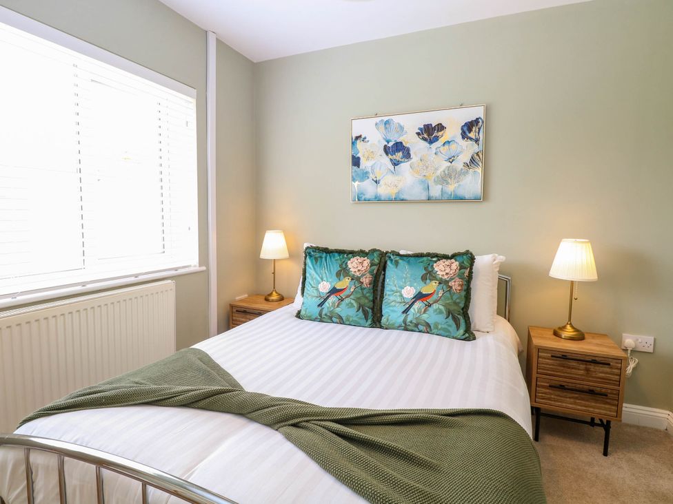 A bedroom with a bed two bedside tables with lamps and a floral painting above the bed at Little Lodge in Dersingham