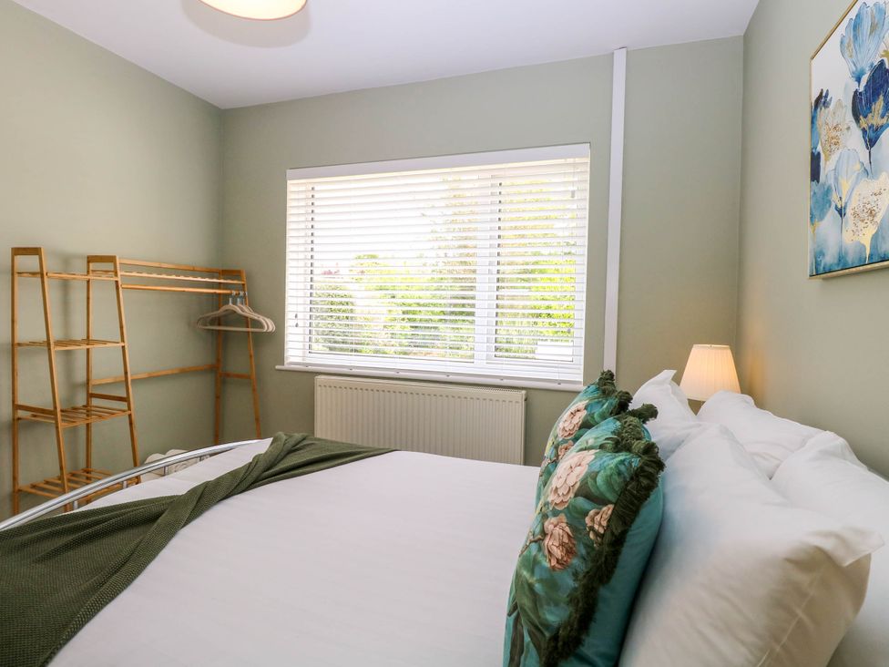 A bedroom with a bed with floral pillows a wooden clothes rack and a window with blinds at Little Lodge in Dersingham