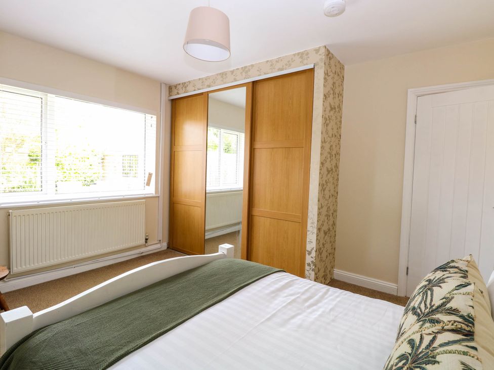 A bedroom with a bed a green blanket a window with blinds a radiator and a mirrored wardrobe at Little Lodge in Dersingham