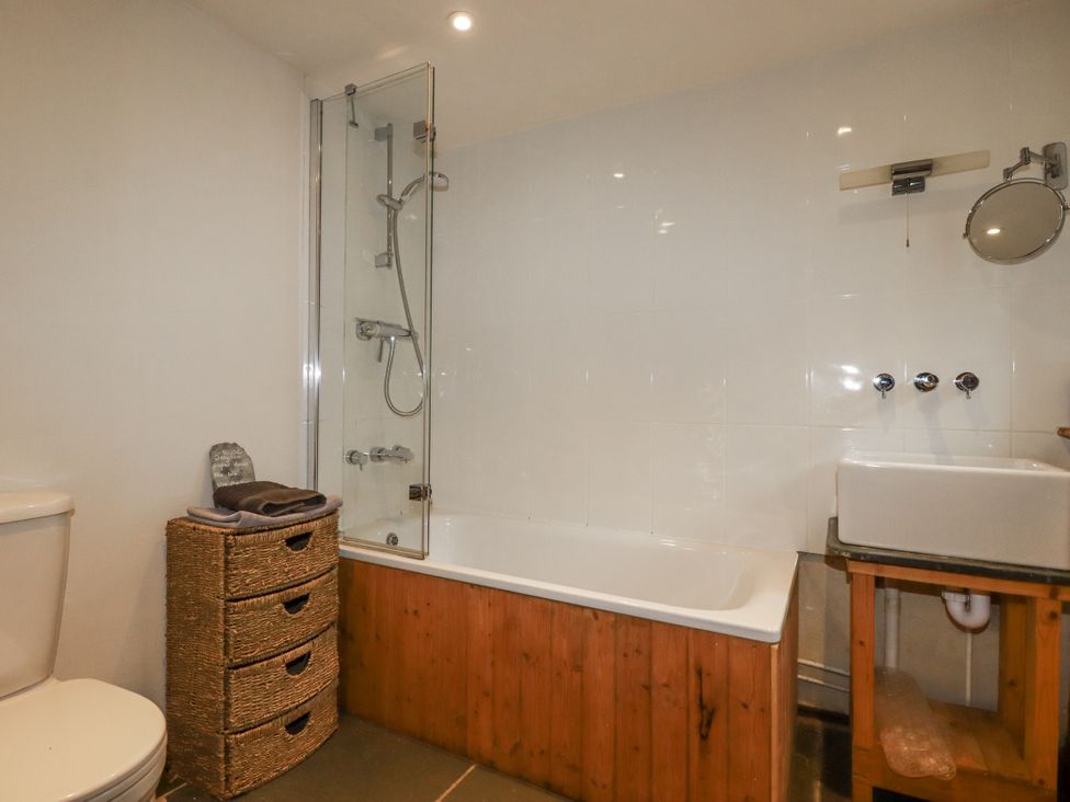 A bathroom featuring a toilet, bathtub with shower, and storage basket at Coombe Barn in Cusgarne near St Day