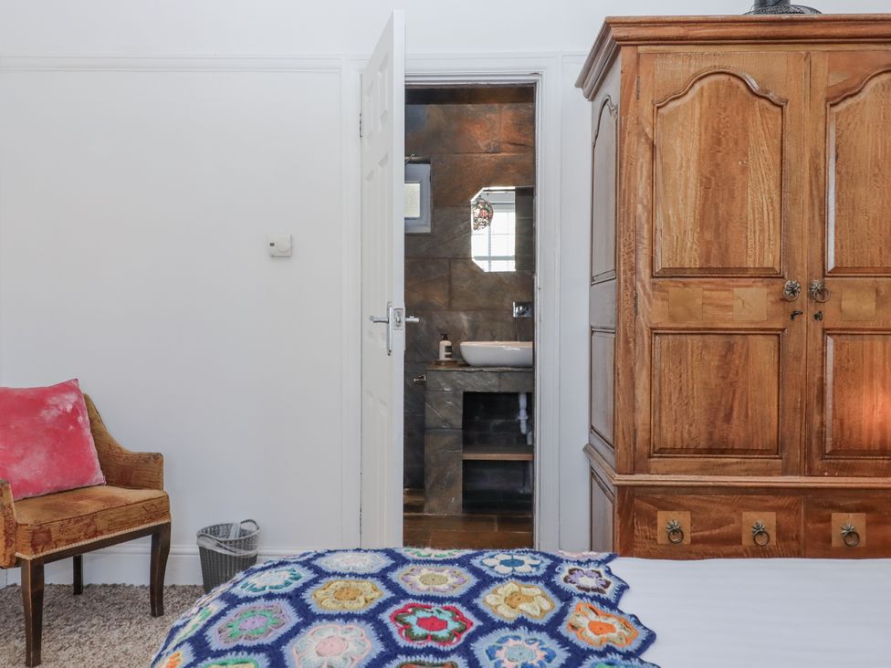 A bedroom with a wardrobe and chair leading to a bathroom at Delmonte Lodge in Torquay