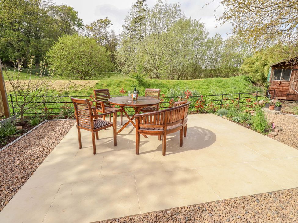 A garden with a wooden table and chairs at The Lodge in Powburn