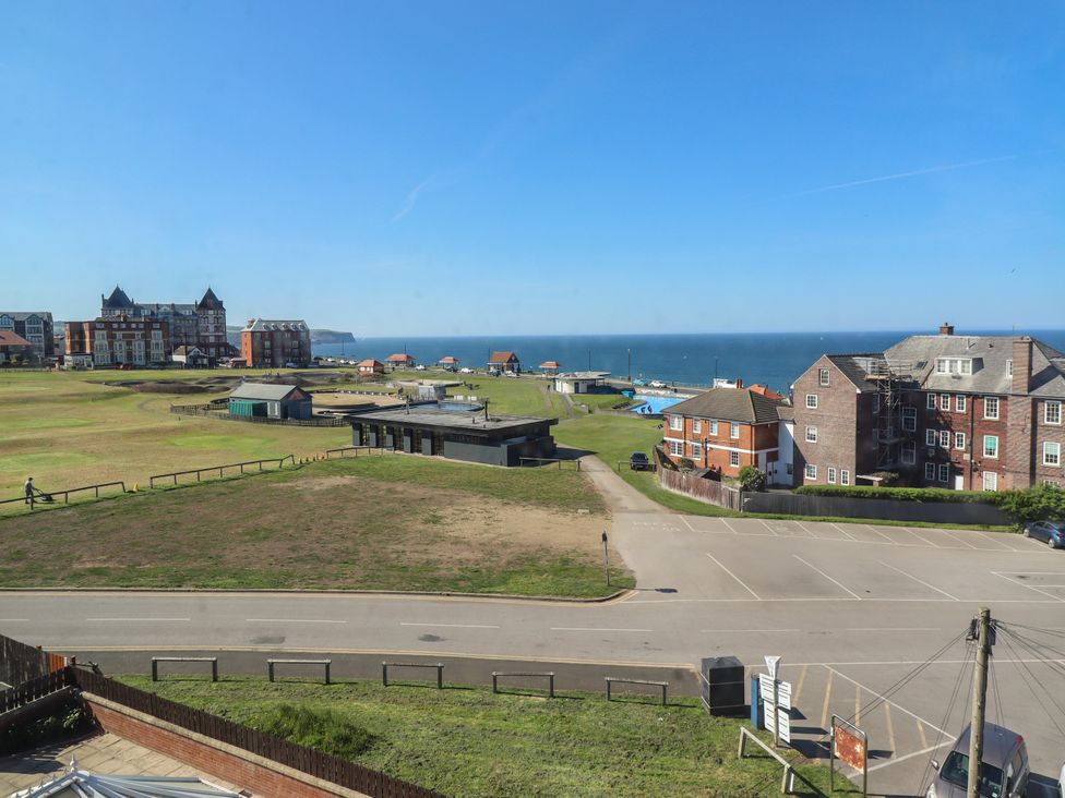 A coastal view with a grassy area, buildings, parking lot, and the sea at Mamoir's Place in Whitby