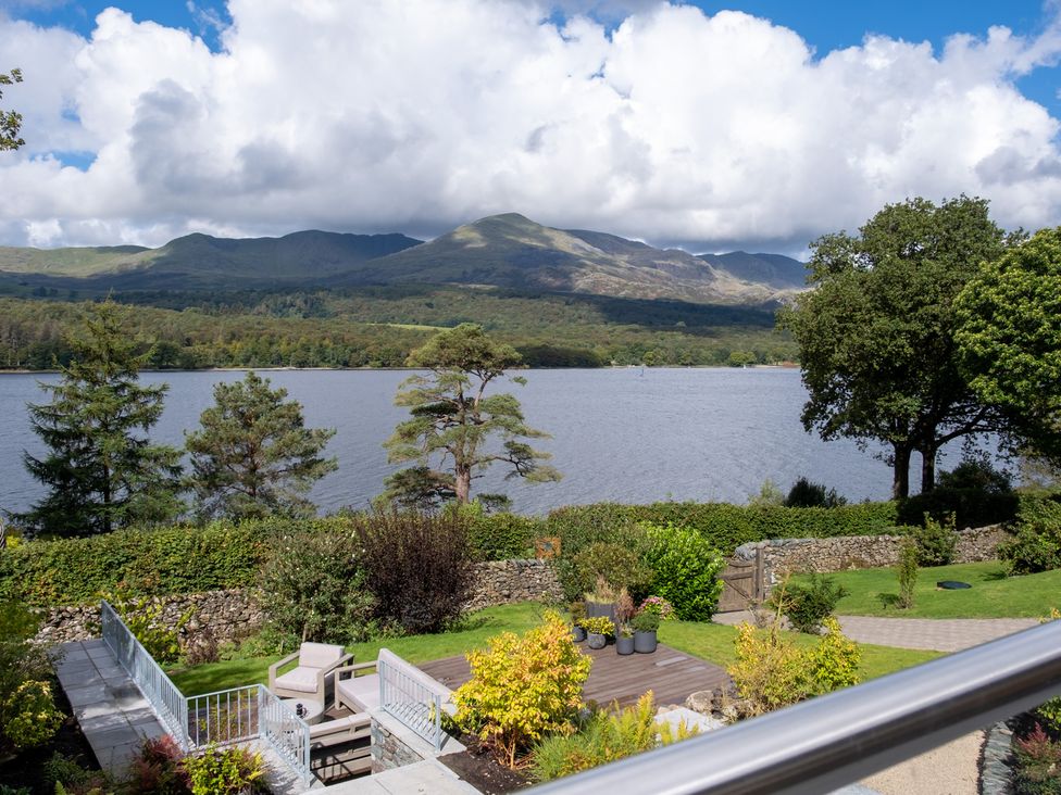 A view of a lake and mountains with trees and a patio at Deer Close in Coniston