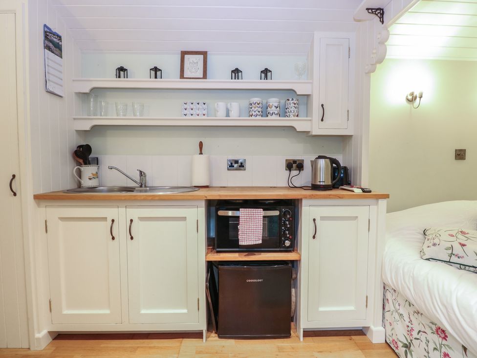 A kitchen area with sink, microwave, kettle, and shelves at Woodlands Retreat Shepherd's Hut Brundish near Laxfield