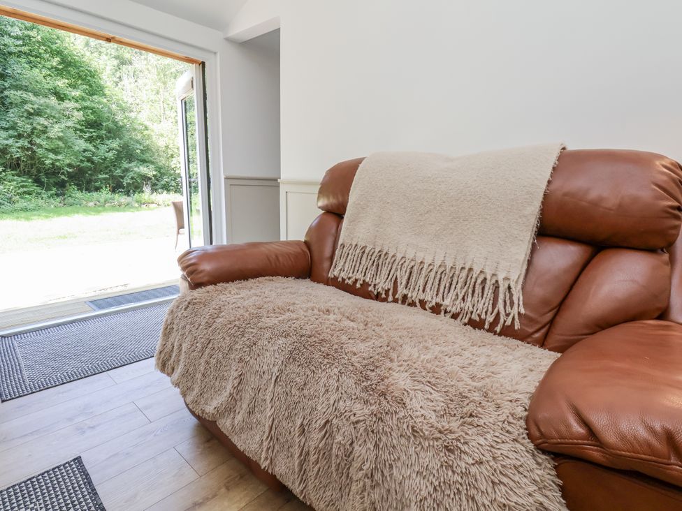 A sofa with a throw blanket in front of a sliding door at Roe Deer Lodge Littlebeck near Sleights
