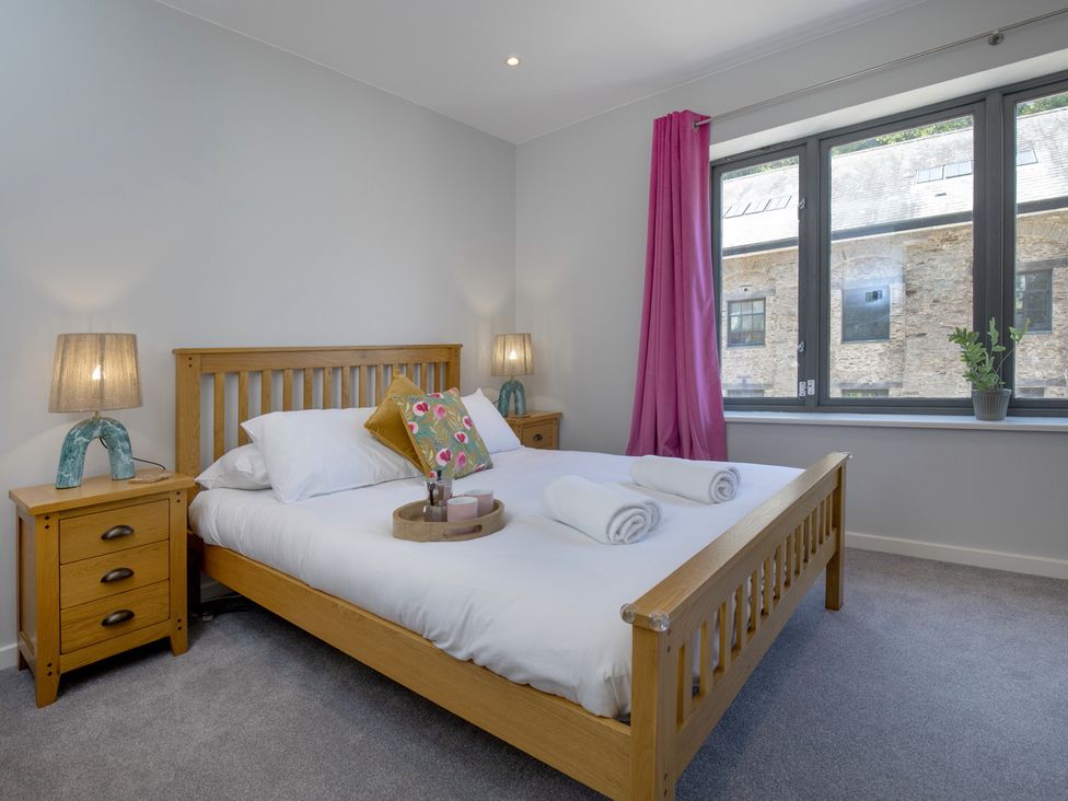 A bedroom with a bed, nightstand, and window at Mariners Retreat, 8 Pottery Cottages, Dartmouth