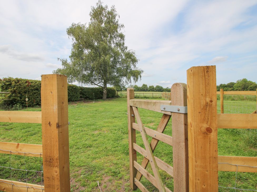 A wooden gate opening to a grassy field with a tree at Old Piggery in Shifnal
