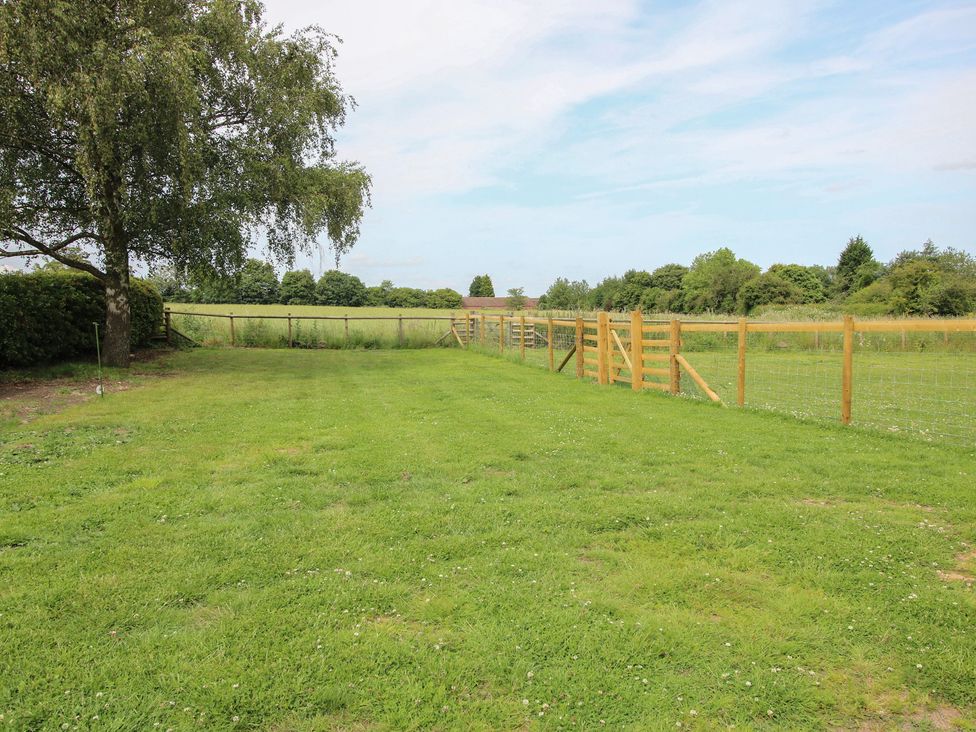 A garden area with grass, a tree, and a wooden fence at The Old Piggery in Shifnal